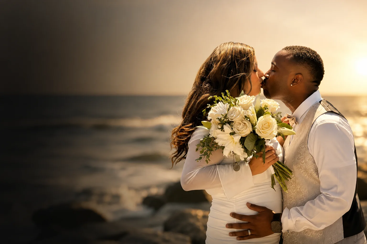 A couple kissing at sunset on the beach, bouquet in hand.